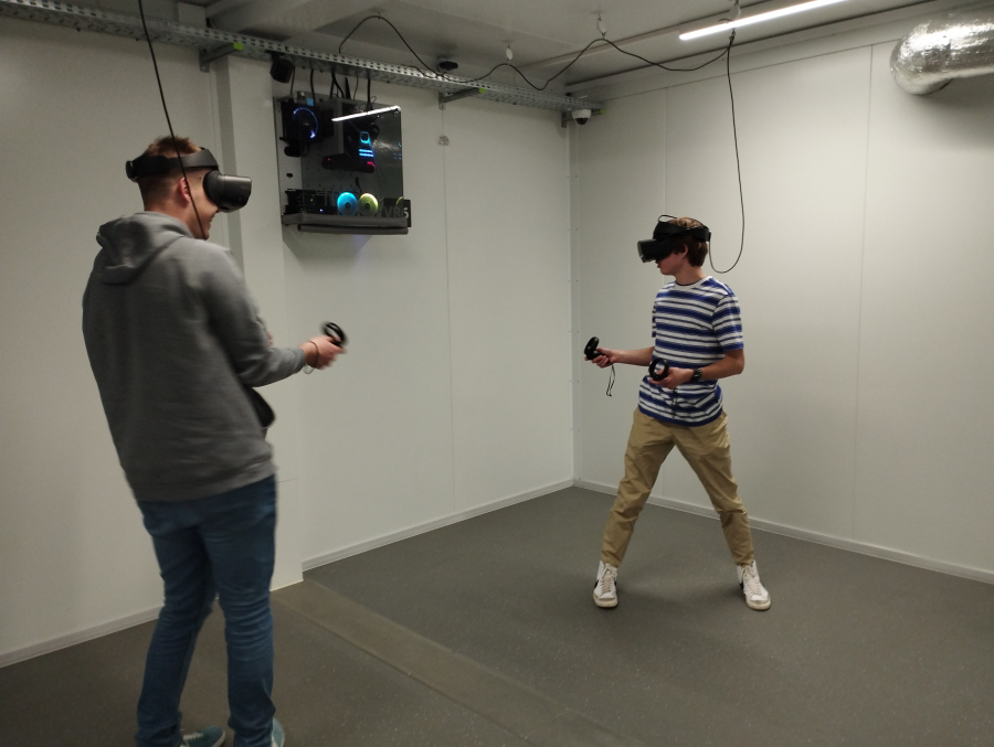 Dwóch mężczyzn korzysta ze strefy VR, nosząc gogle i kontrolery w rękach.